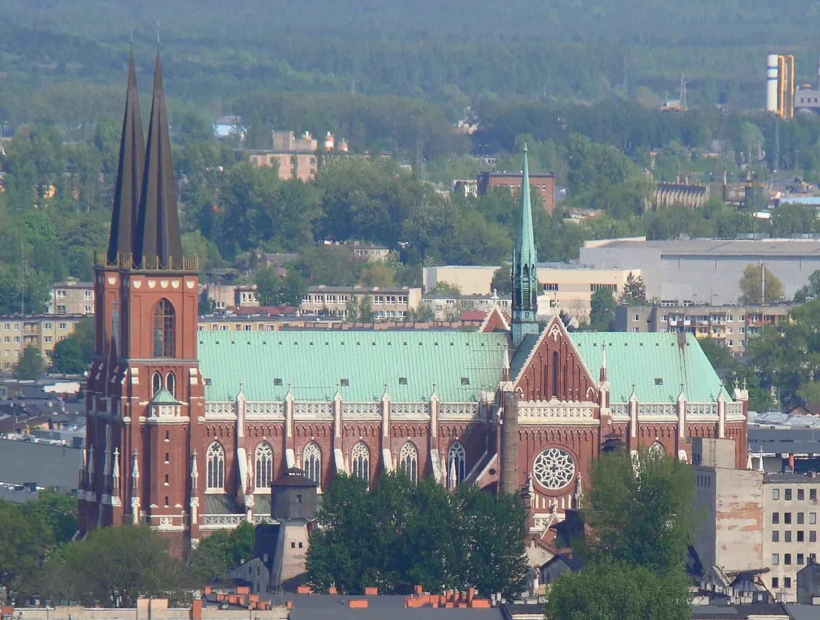 An aerial view of a large, old brick church with a green roof and two tall spires, surrounded by other buildings and trees.