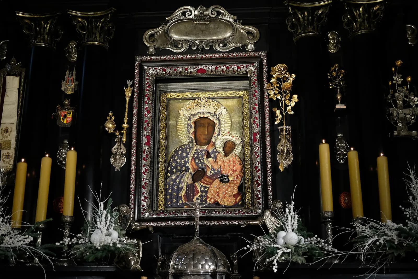 A religious icon of the Black Madonna with Child in a dark setting, surrounded by candles and elaborate decorations.